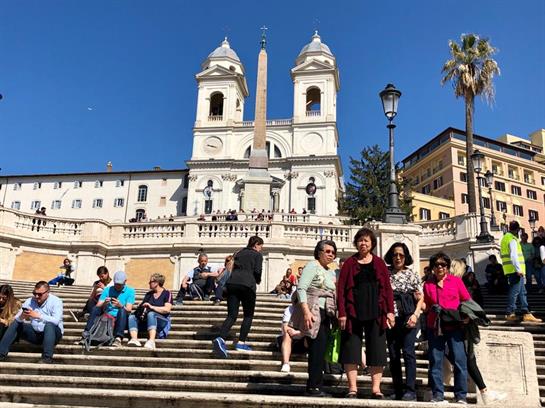 Groups of tourists gather on the Spanish Steps during a sunny day in Rome to enjoy the view.