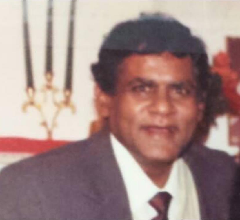 A man dressed in a suit smiles warmly at a social event with festive decorations around him.