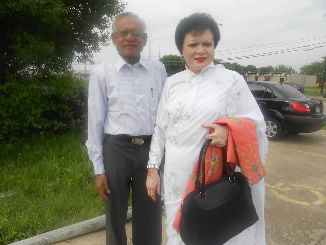 Couple stands together, showcasing elegant traditional attire amidst a cloudy backdrop.