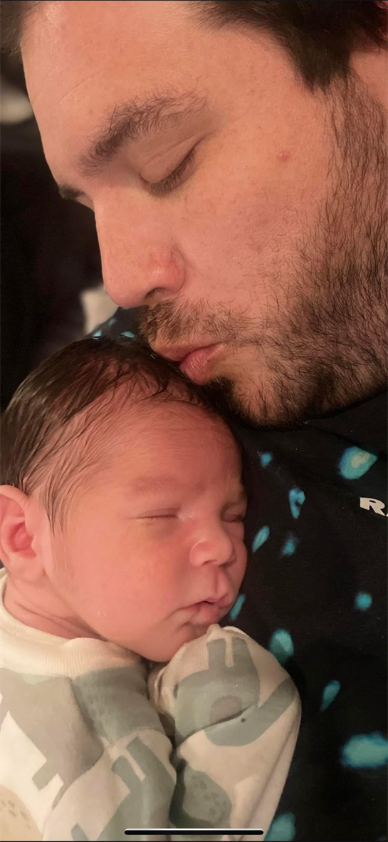 A father kisses his sleeping newborn son, highlighting their deep bond in a cozy home.