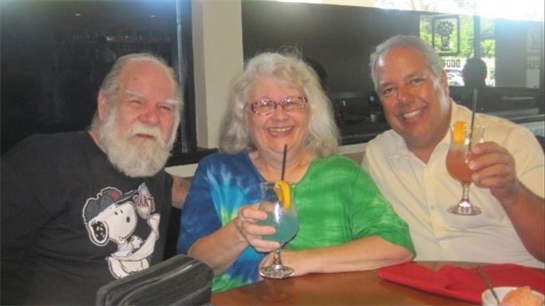 Three friends smile and raise their cocktails at a lively get-together in the afternoon.