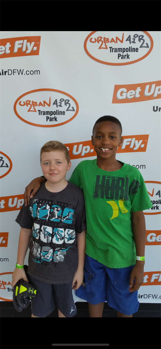 Two young boys smile together at an indoor trampoline park, showcasing their playful moment.