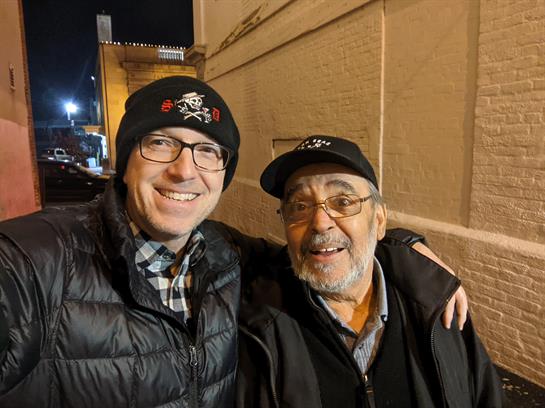 Two men pose joyfully together in an urban area during a night outing filled with camaraderie.