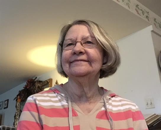 An elderly woman with glasses is smiling warmly in a bright, inviting room filled with warmth.