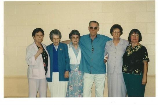 Six elderly friends stand close together, smiling warmly during a social gathering.