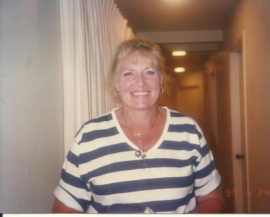 A cheerful woman with blonde hair stands in a hallway, exuding warmth and friendliness.