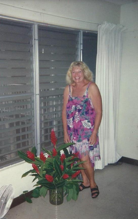 A woman stands smiling beside a colorful flower arrangement in a well-lit room.