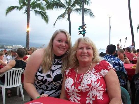 Two women in vibrant outfits smile at a table during a lively evening gathering.