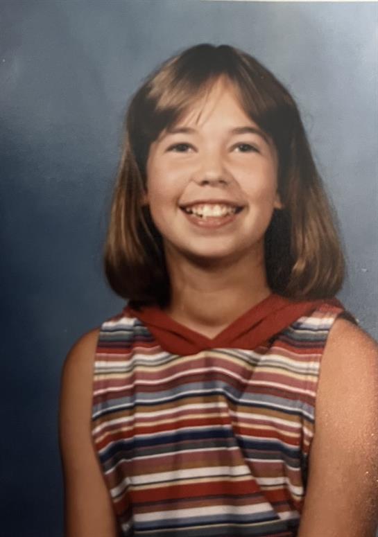 Young girl with bobbed hair smiles brightly while wearing a striped dress in a studio setting.
