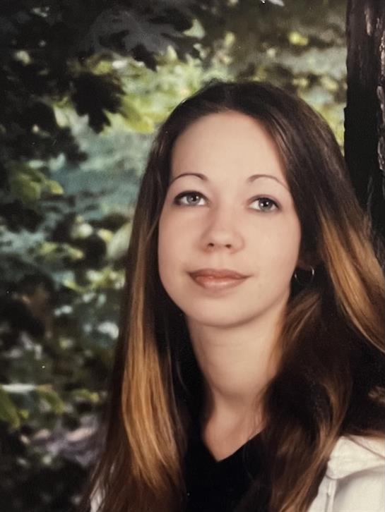A young woman stands against a tree, smiling softly in a vibrant green park setting.