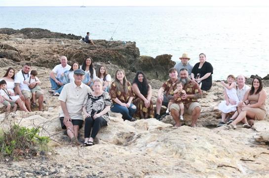 A large family enjoys each other's company by the rocky shore as the sun sets over the ocean.
