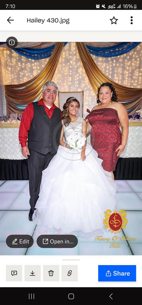 A girl in a white gown stands with her parents, celebrating her quinceanera in a festive venue.