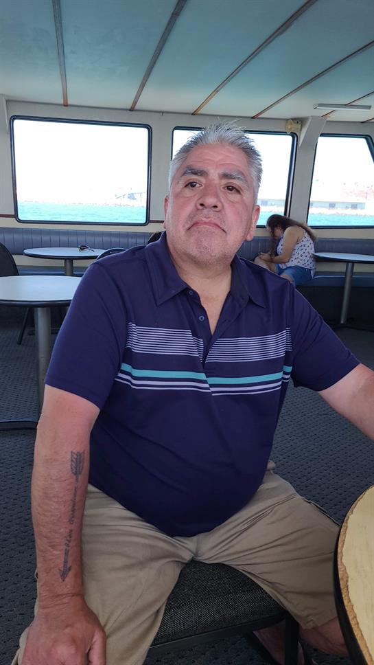 A man is seated at a table inside a boat, looking towards the camera with a relaxed expression.