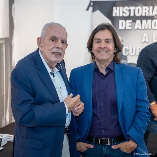Two men in matching blue suits chat warmly during a book signing event held in Cuba.