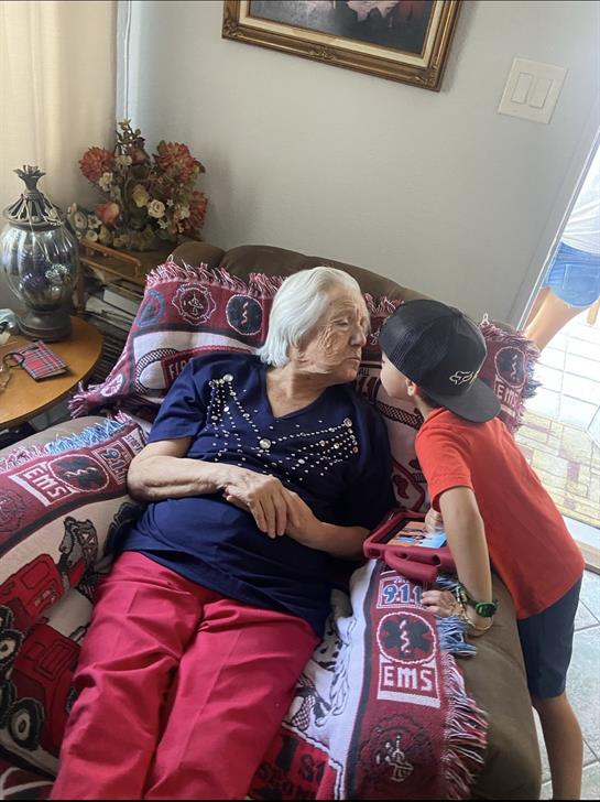 A young boy kisses an elderly woman on a couch, showing affection in a cozy living room.