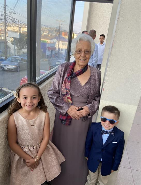 Grandmother stands proudly with two smiling children in a bright hallway with a view.