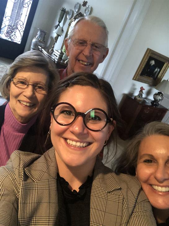 Four family members smile happily together in a cozy living room setting, enjoying their time.