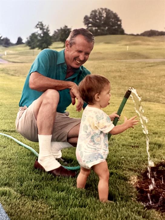 A cheerful grandfather helps his grandson water the garden on a sunny day.