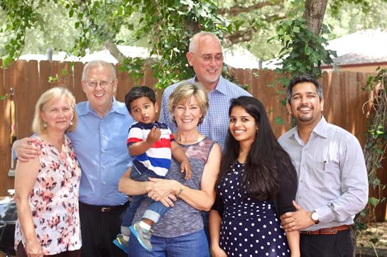 A cheerful family poses for a photo in a lush garden filled with trees on a bright day.