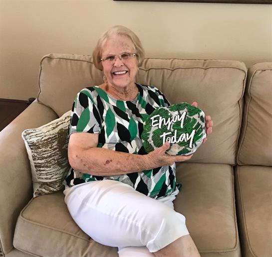 Elderly woman enjoys holding a stone that reads Enjoy Today while sitting on a couch.
