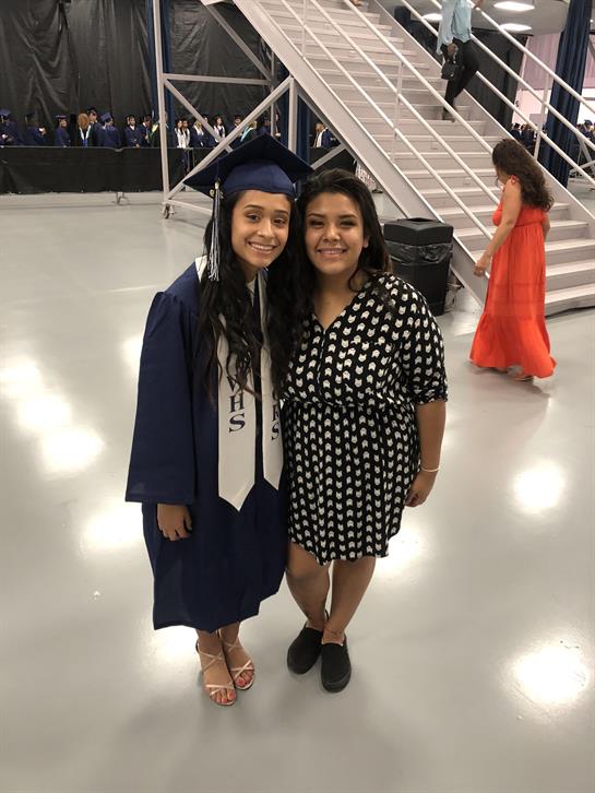 Two friends pose joyfully together during a graduation celebration at an indoor venue.