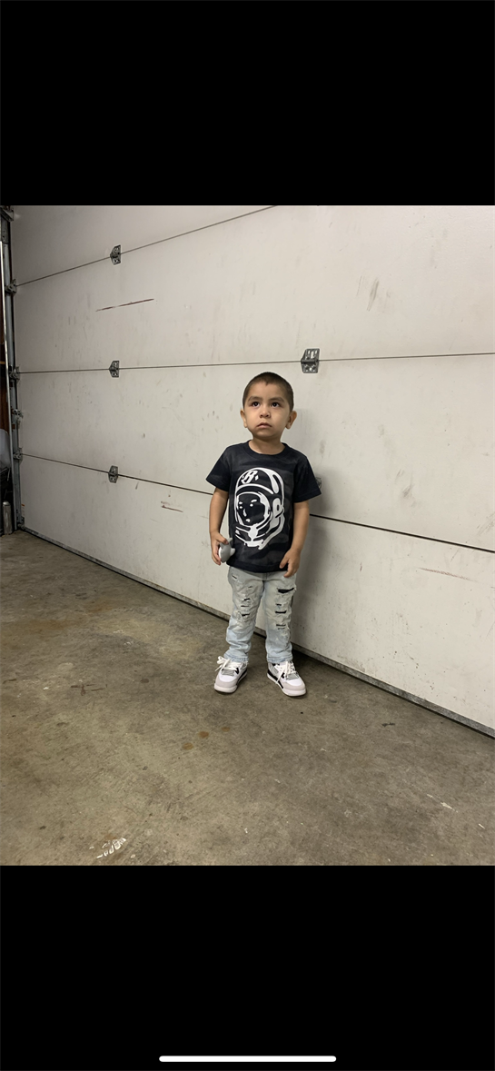 Young child poses in a garage, showcasing his stylish outfit and confident demeanor.