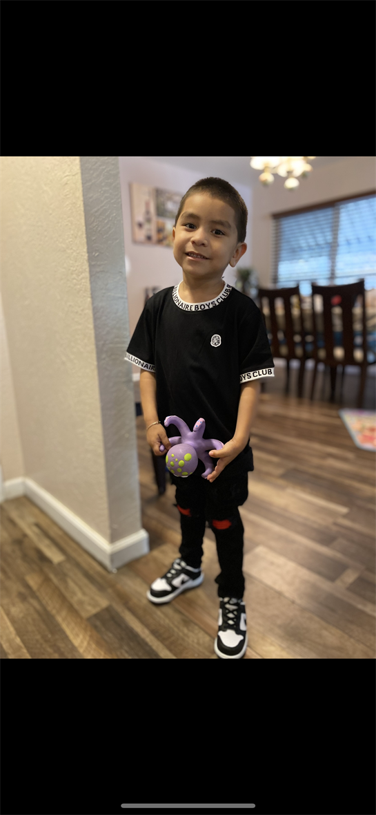 A child smiles while standing in a cozy living room, holding a vibrant purple toy.