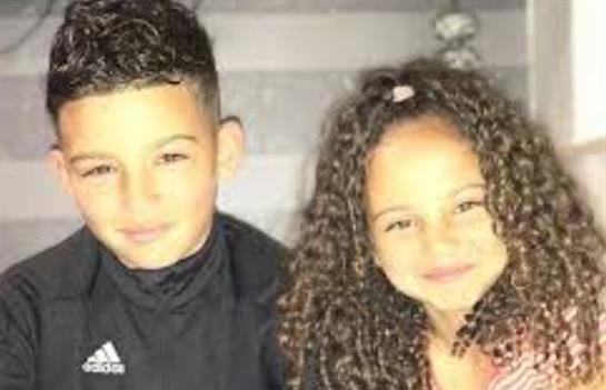 Two children are sitting closely together, sharing smiles in a warm, inviting space.