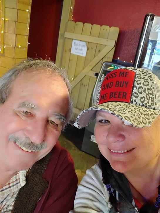 Two individuals smile cheerfully while posing together, showcasing hats and jovial expressions.