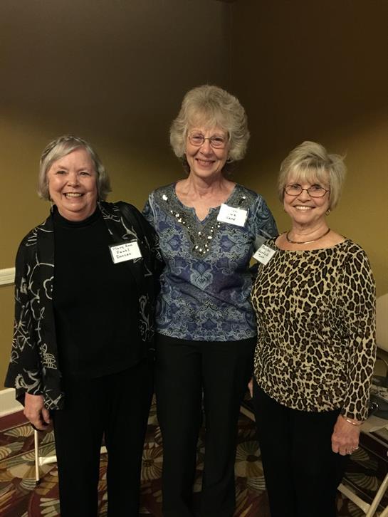 Three elderly women enjoy each other's company at a lively social gathering.