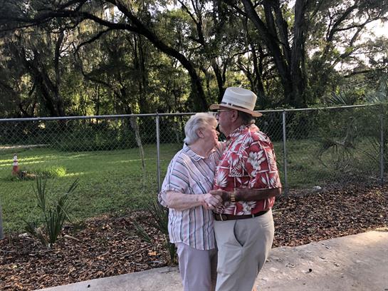 A happy elderly couple shares a tender moment dancing together outside surrounded by greenery.