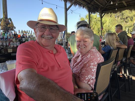 A cheerful couple sits close together, savoring drinks at a lively outdoor bar.