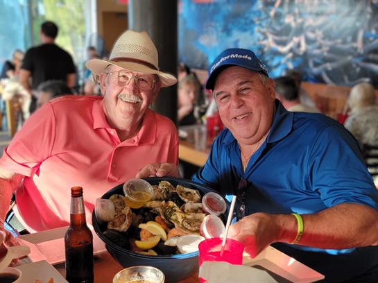 Friends share laughter and seafood at a lively coastal restaurant filled with patrons.