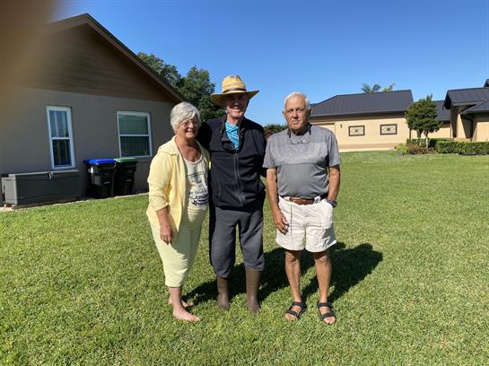 Three friends celebrate their time together in a sunny outdoor setting with lush grass.