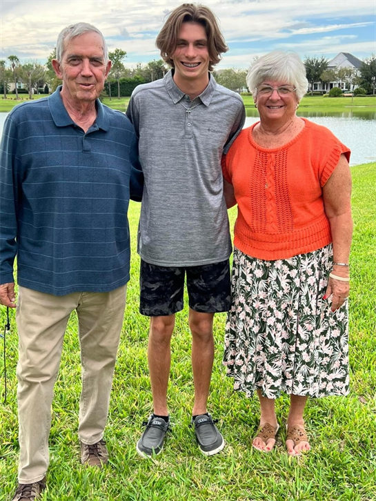 Three family members stand together by a tranquil lake on a sunny day.