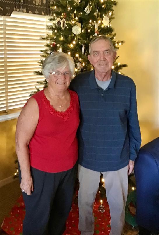 Two elderly individuals enjoy a warm moment by a brightly lit Christmas tree.
