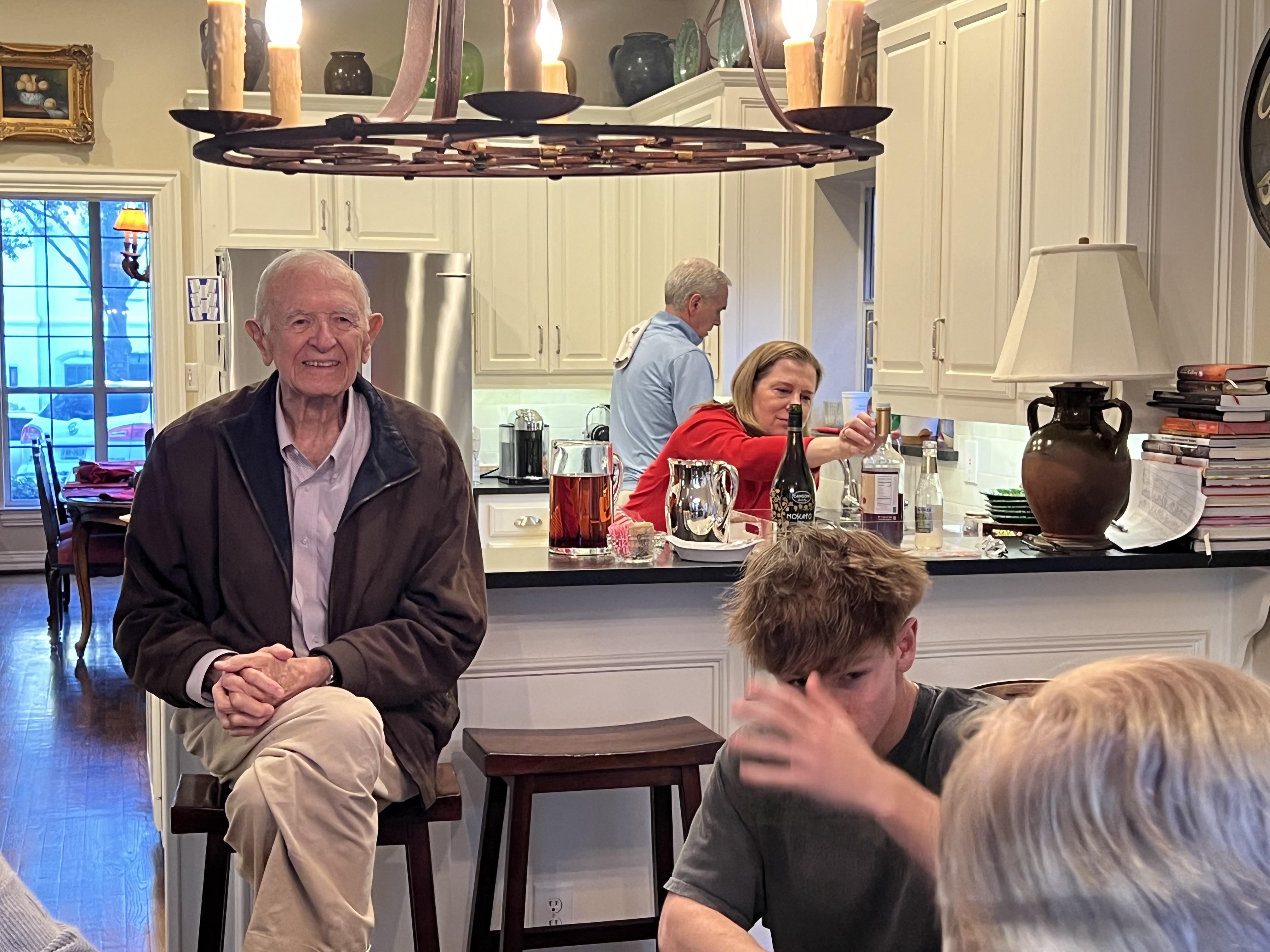 Elderly man enjoys time with family as they prepare food and share stories in a warm kitchen.