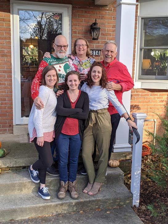 A joyful family poses together on the porch, showcasing holiday spirit and warmth.