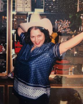 A joyful woman wearing a cowboy hat poses playfully indoors surrounded by musical instruments.