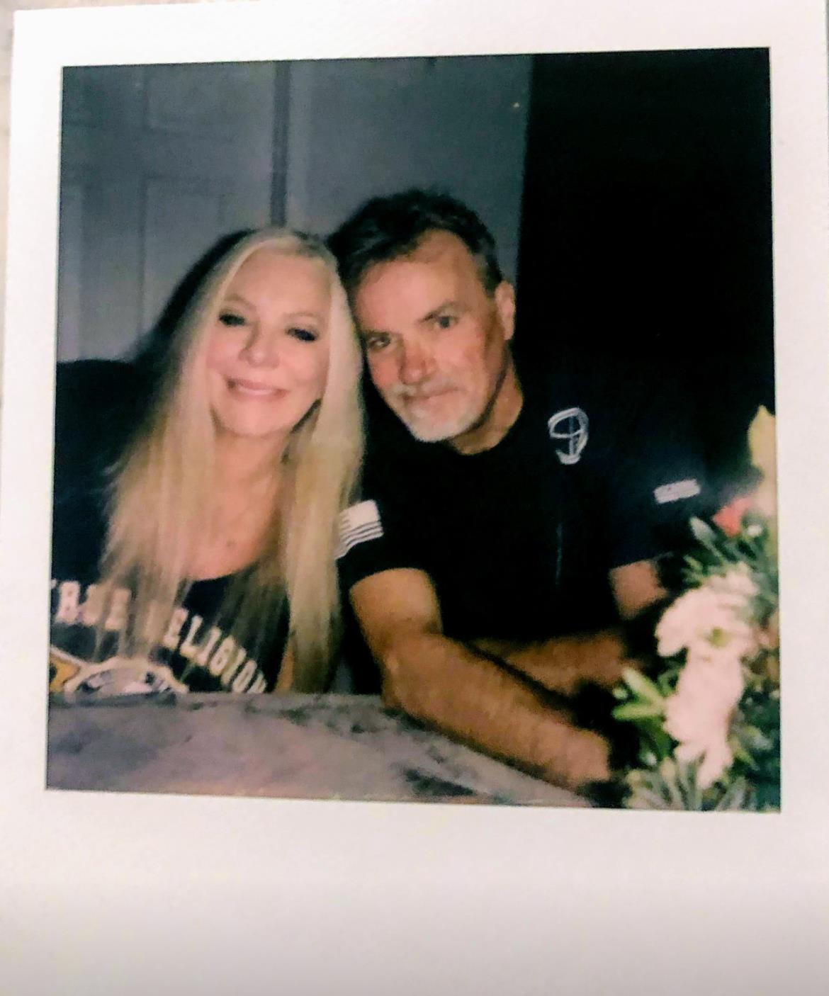Happy couple poses closely at a table with flowers during a relaxed gathering in the evening.