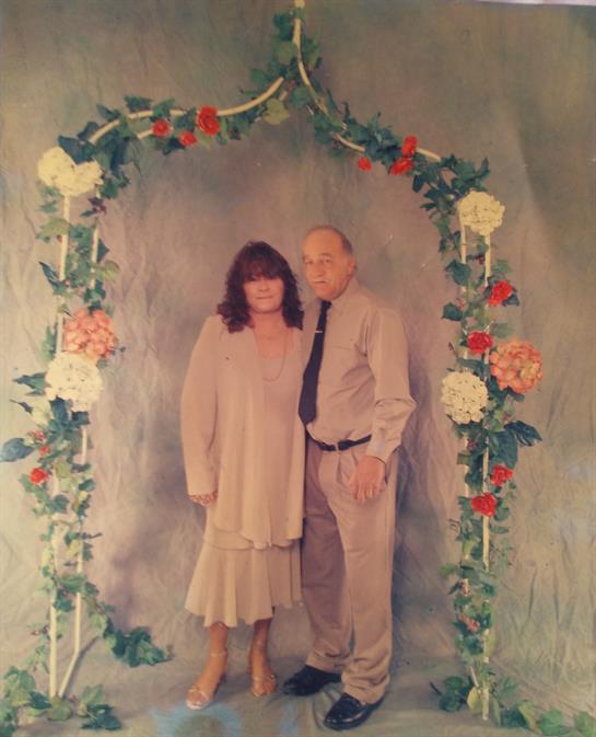 A couple stands together under a decorated floral arch, radiating joy and affection.