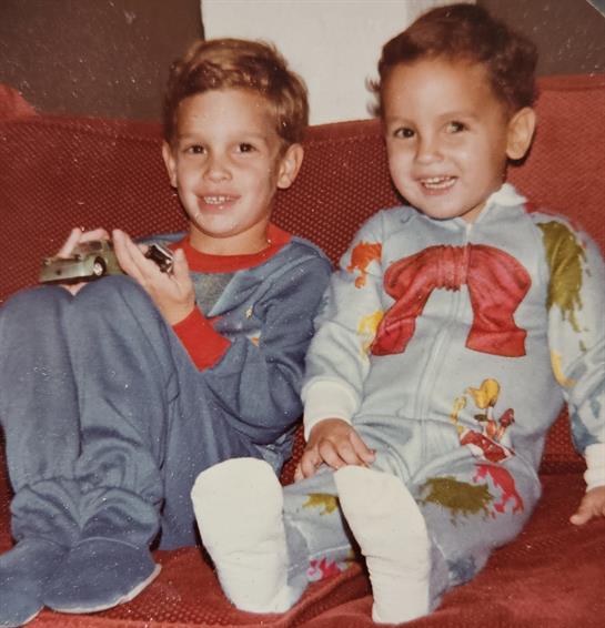 Two young boys sit together on a couch, sharing laughter while playing with toys in their pajamas.