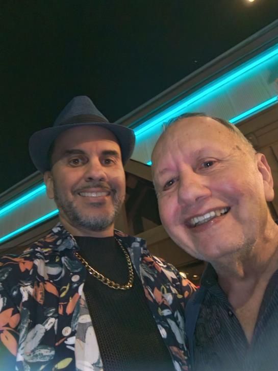 Two friends smile for a friendly selfie at a lively venue adorned with colorful lights.