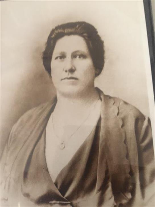 A woman dressed in vintage clothing poses with a neutral expression, showcasing her style.