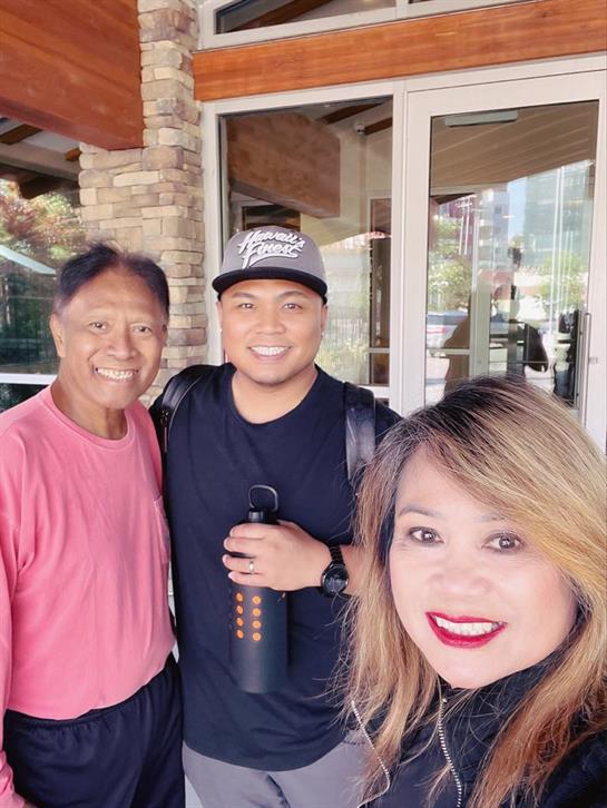 Three friends smiling together outside an attractive building, enjoying a sunny day.