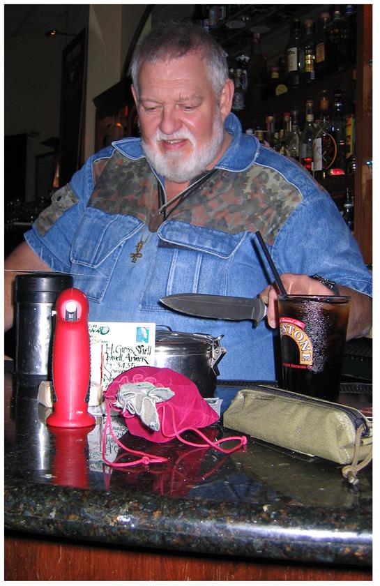 A man enjoys time at a bar with drinks and personal items on the counter, displaying a knife.