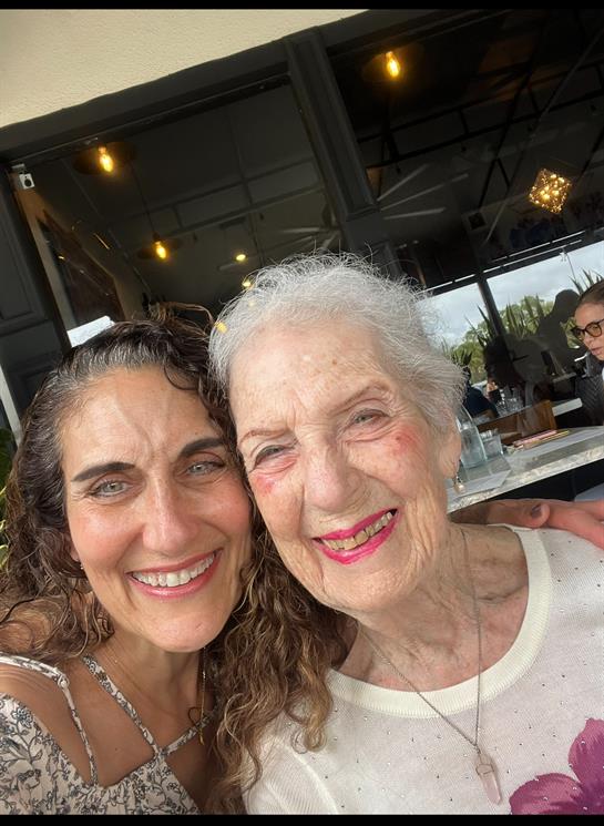 Two women enjoy a joyful moment at a cafe, sharing smiles and laughter in the sunlight.