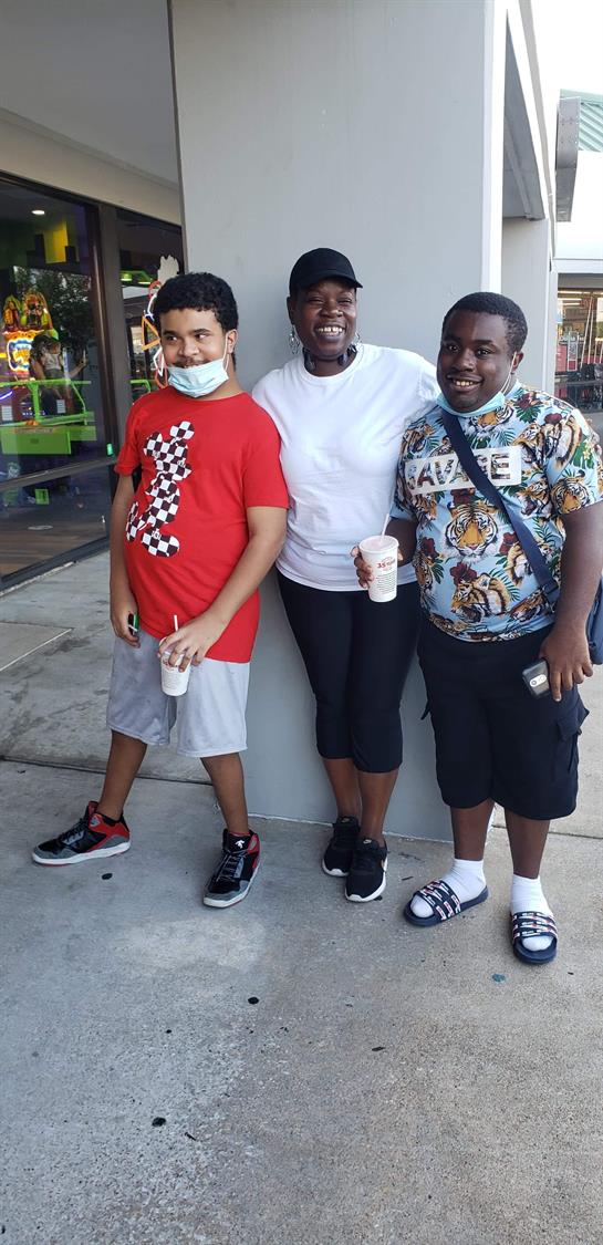 Three friends stand together outside a fun center, sipping cold drinks and smiling.