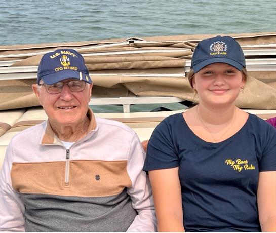 A cheerful grandfather and granddaughter share smiles as they relax on a boat in warm weather.