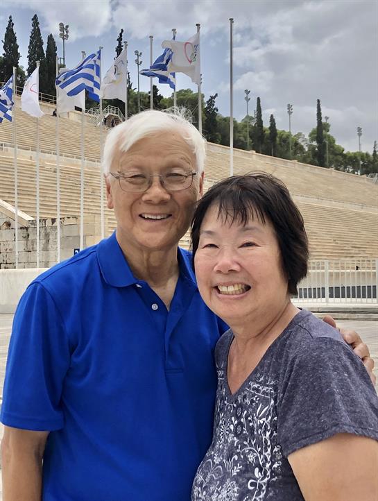 Happy couple poses in front of impressive stone architecture with flags waving in the background.